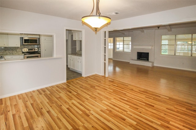 unfurnished living room featuring a brick fireplace and light hardwood / wood-style flooring