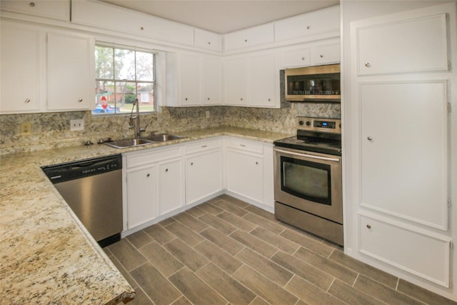 kitchen featuring tasteful backsplash, light stone counters, stainless steel appliances, sink, and white cabinets