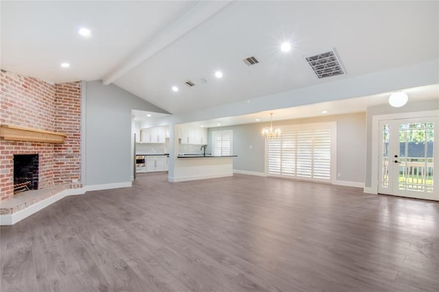 unfurnished living room featuring lofted ceiling with beams, sink, wood-type flooring, and a brick fireplace