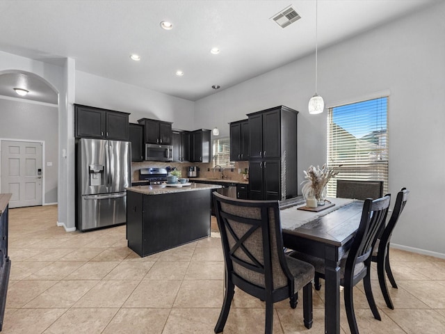 kitchen featuring light stone countertops, stainless steel appliances, sink, decorative light fixtures, and a kitchen island