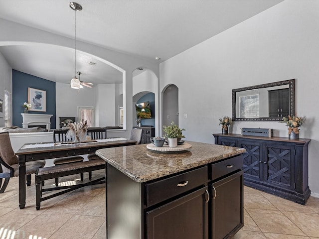 kitchen featuring ceiling fan, a kitchen island, pendant lighting, stone countertops, and light tile patterned flooring