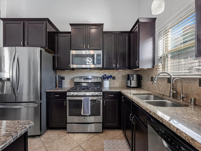 kitchen with appliances with stainless steel finishes, light stone counters, dark brown cabinets, sink, and light tile patterned floors