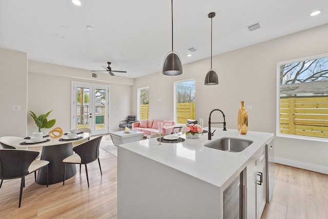 kitchen featuring pendant lighting, a kitchen island with sink, sink, ceiling fan, and light wood-type flooring