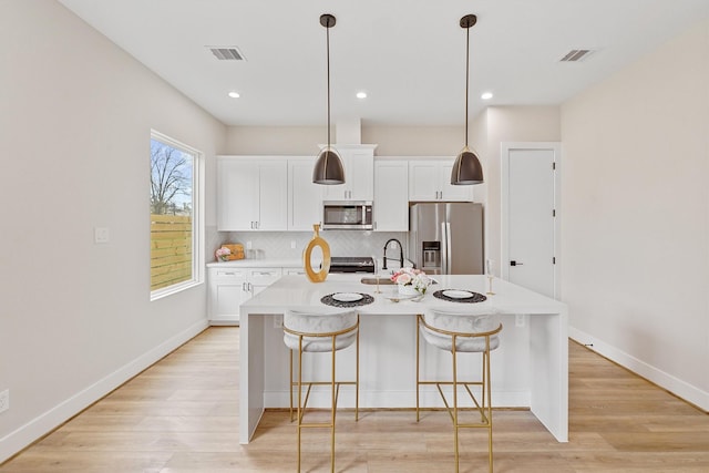 kitchen featuring decorative backsplash, stainless steel appliances, a kitchen island with sink, decorative light fixtures, and white cabinets