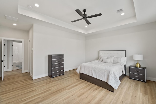 bedroom featuring light wood-type flooring, a tray ceiling, and ceiling fan