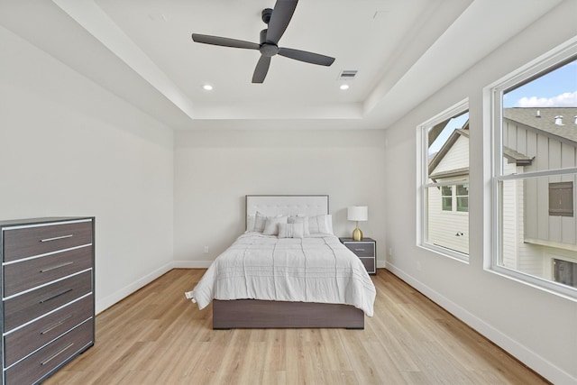 bedroom featuring ceiling fan, light wood-type flooring, and a tray ceiling