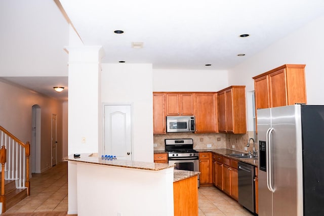 kitchen featuring a center island, sink, stainless steel appliances, light stone counters, and light tile patterned floors