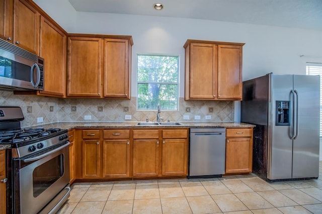 kitchen featuring light stone countertops, sink, tasteful backsplash, light tile patterned flooring, and appliances with stainless steel finishes