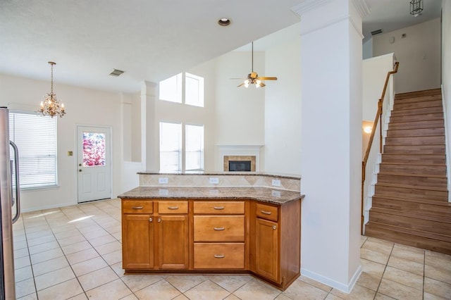 kitchen with a tile fireplace, light stone countertops, light tile patterned flooring, and ceiling fan with notable chandelier