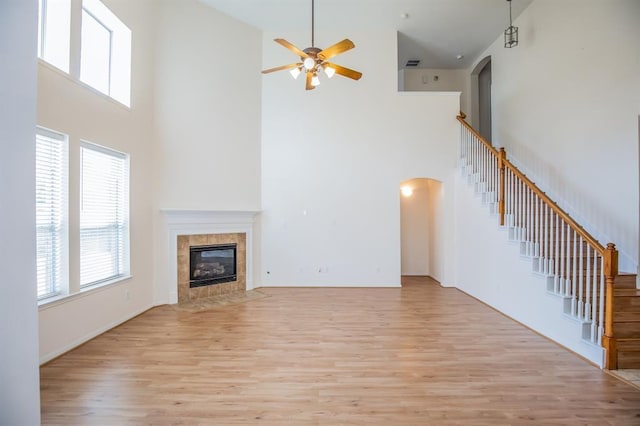 unfurnished living room with a tile fireplace, a high ceiling, light hardwood / wood-style floors, and ceiling fan