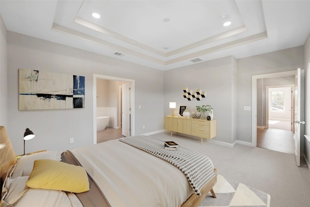 carpeted bedroom with connected bathroom and a tray ceiling