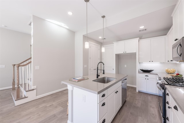 kitchen with sink, hanging light fixtures, an island with sink, white cabinets, and appliances with stainless steel finishes