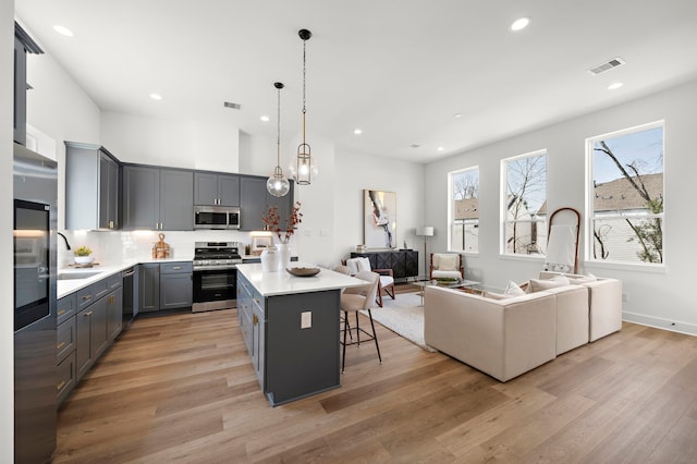 kitchen with stainless steel appliances, gray cabinets, hanging light fixtures, and light hardwood / wood-style flooring