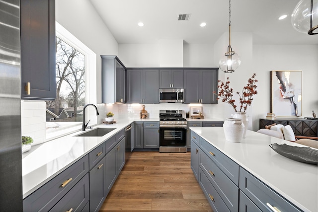 kitchen featuring pendant lighting, sink, gray cabinetry, stainless steel appliances, and dark hardwood / wood-style flooring