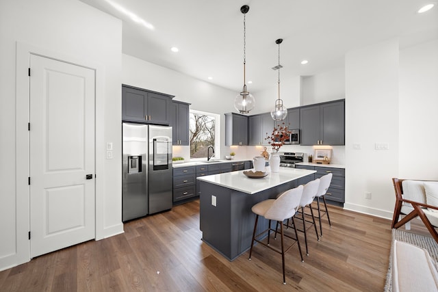 kitchen featuring pendant lighting, sink, appliances with stainless steel finishes, a center island, and a kitchen bar