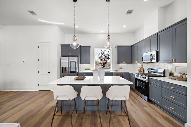 kitchen with pendant lighting, stainless steel appliances, a center island, wood-type flooring, and decorative backsplash