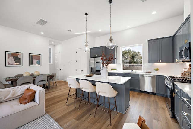 kitchen featuring wood-type flooring, hanging light fixtures, a kitchen island, stainless steel appliances, and decorative backsplash