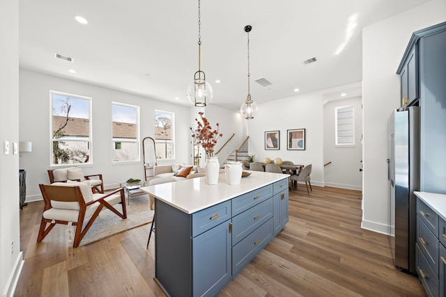 kitchen featuring pendant lighting, hardwood / wood-style floors, stainless steel refrigerator, and blue cabinets