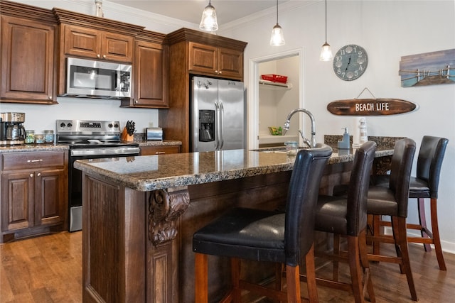 kitchen with stainless steel appliances, crown molding, hardwood / wood-style floors, an island with sink, and a breakfast bar