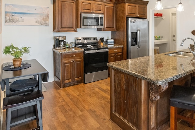 kitchen featuring sink, dark stone countertops, pendant lighting, light hardwood / wood-style floors, and appliances with stainless steel finishes