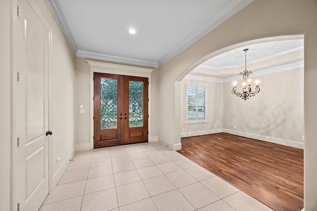 tiled entryway featuring french doors, ornamental molding, and a notable chandelier