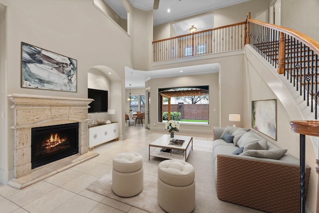 living room with a tile fireplace, a high ceiling, light tile patterned floors, and crown molding