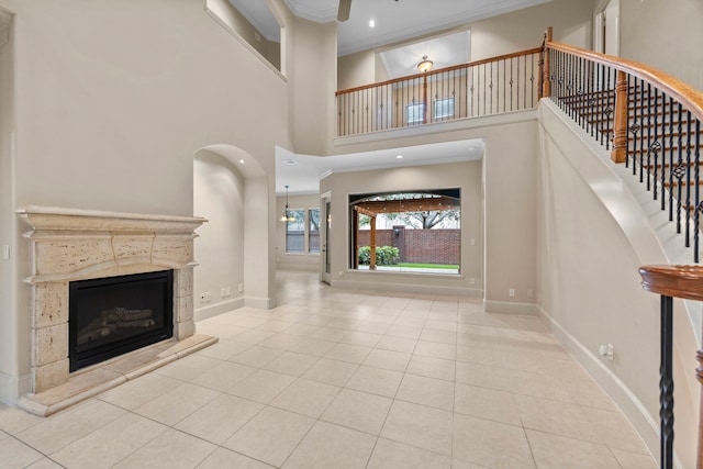 unfurnished living room with a tiled fireplace, light tile patterned floors, a high ceiling, and ornamental molding