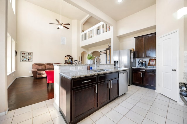 kitchen featuring light tile patterned floors, a center island with sink, stainless steel appliances, dark brown cabinets, and sink