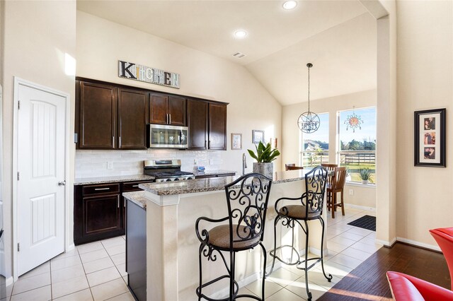 kitchen featuring vaulted ceiling, a kitchen island with sink, stove, stone counters, and pendant lighting