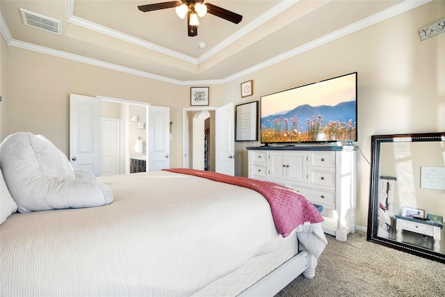 carpeted bedroom featuring ceiling fan, ornamental molding, a tray ceiling, and ensuite bath