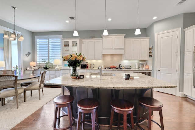 kitchen with a kitchen island with sink, light hardwood / wood-style flooring, a notable chandelier, decorative backsplash, and white cabinets