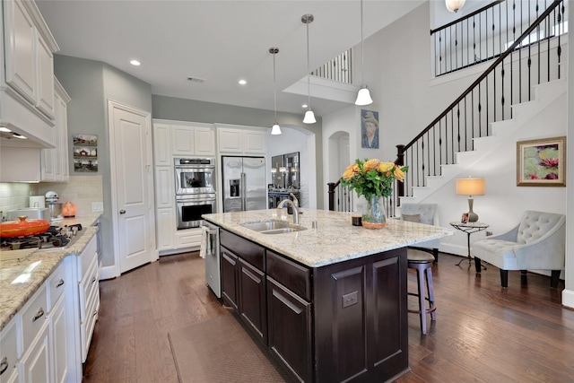 kitchen featuring appliances with stainless steel finishes, a kitchen island with sink, sink, white cabinetry, and a breakfast bar area