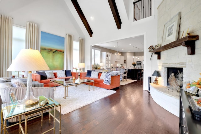 living room with dark wood-type flooring, high vaulted ceiling, a tiled fireplace, beam ceiling, and a chandelier