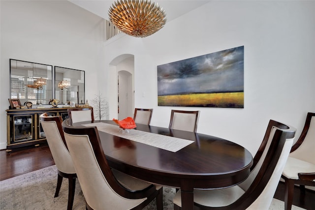 dining area featuring hardwood / wood-style flooring, a towering ceiling, and a notable chandelier