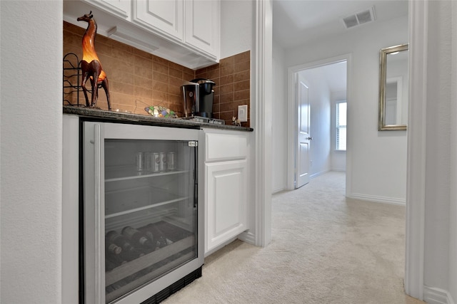 bar with backsplash, wine cooler, white cabinetry, and light carpet