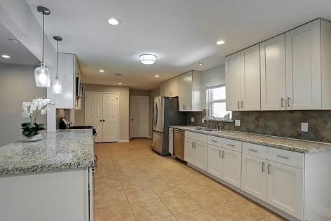 kitchen with light stone countertops, decorative light fixtures, decorative backsplash, white cabinets, and appliances with stainless steel finishes