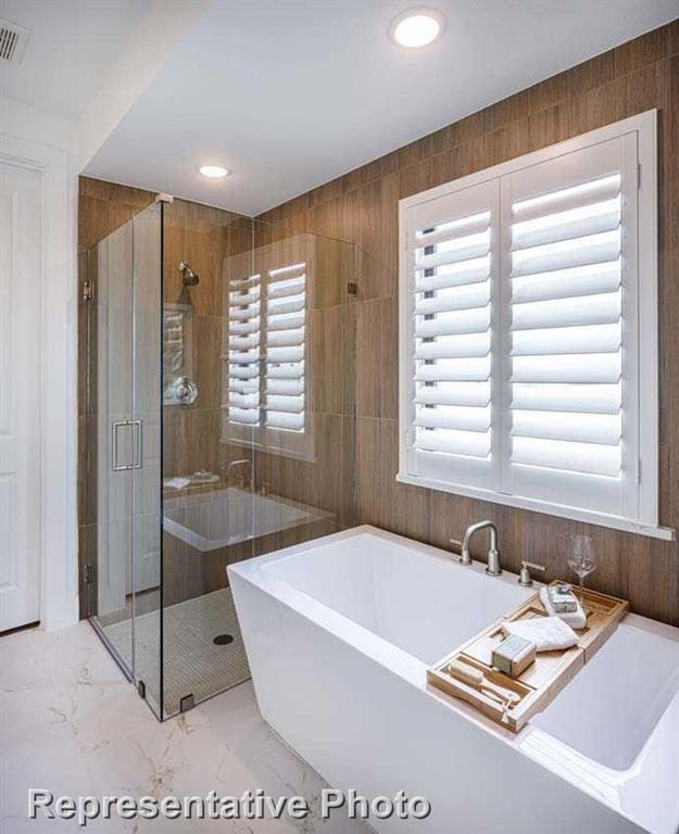 full bathroom with plenty of natural light, marble finish floor, a freestanding bath, and a shower stall