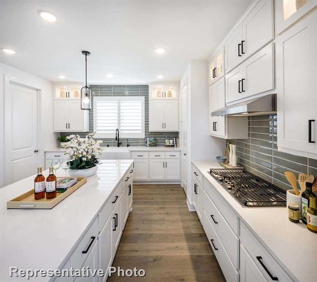 kitchen featuring under cabinet range hood, white cabinetry, light countertops, glass insert cabinets, and stainless steel gas cooktop