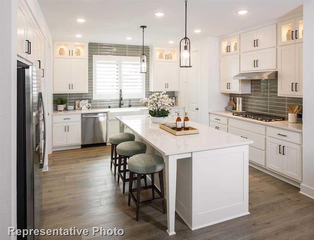 kitchen featuring a center island, under cabinet range hood, a kitchen bar, appliances with stainless steel finishes, and white cabinetry