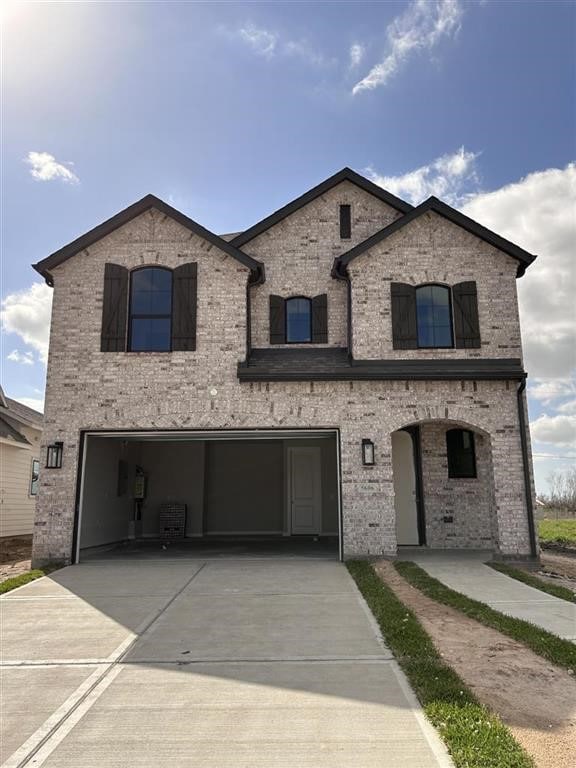 french provincial home featuring concrete driveway, an attached garage, and brick siding