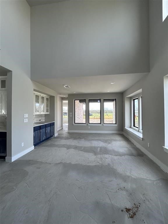 unfurnished living room with baseboards, concrete flooring, and a towering ceiling