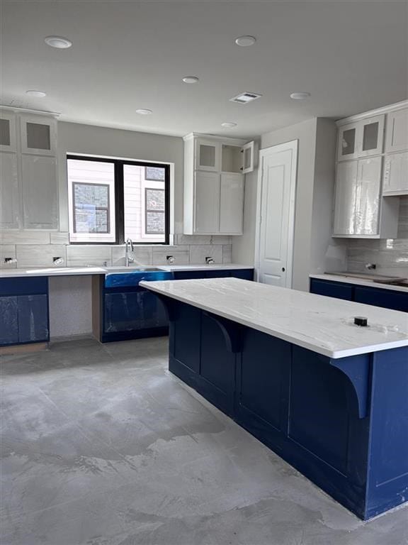 kitchen featuring tasteful backsplash, visible vents, a kitchen island, glass insert cabinets, and a breakfast bar area