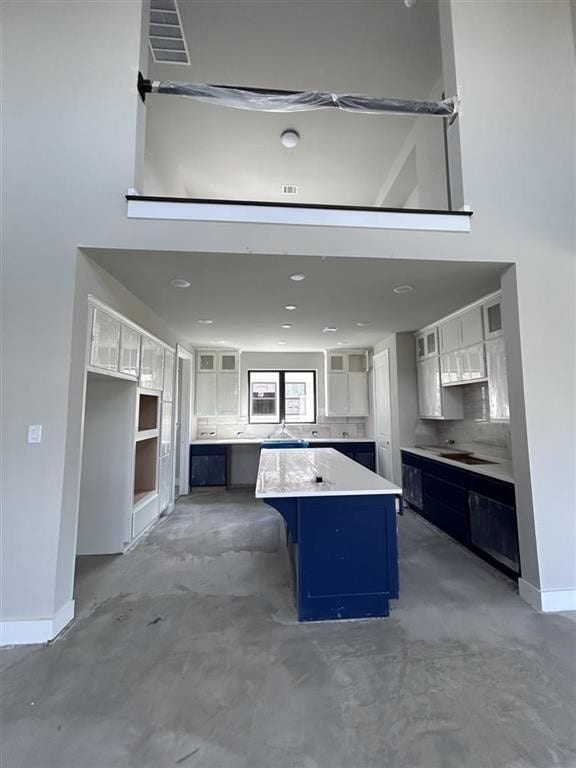 kitchen featuring a kitchen island, glass insert cabinets, concrete floors, baseboards, and blue cabinets