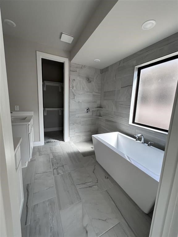 full bathroom featuring vanity, a freestanding tub, a tile shower, a walk in closet, and marble finish floor