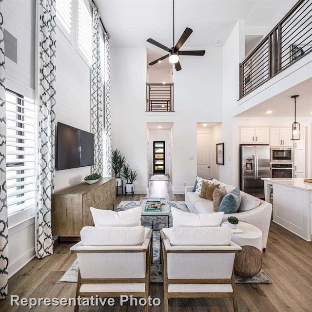 living area with baseboards, a high ceiling, a ceiling fan, and wood finished floors