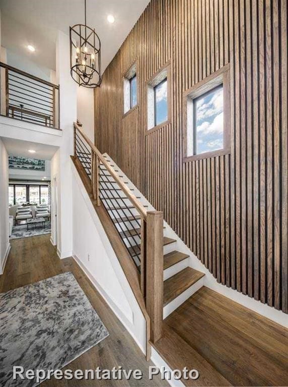 stairway with recessed lighting, an inviting chandelier, wood finished floors, and a towering ceiling