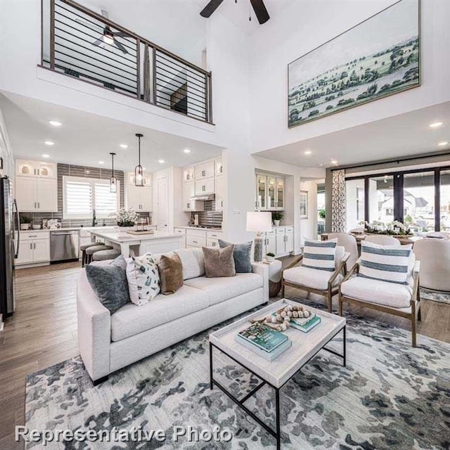 living area featuring a ceiling fan, recessed lighting, wood finished floors, and a towering ceiling