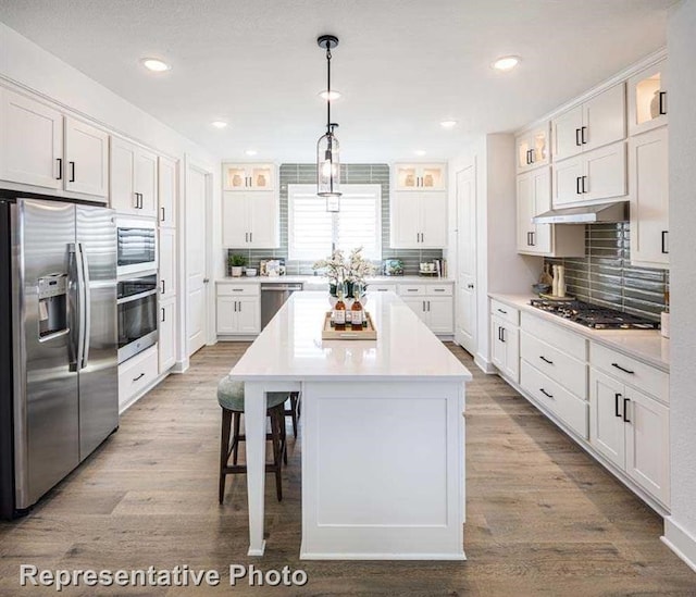 kitchen with wood finished floors, white cabinets, glass insert cabinets, under cabinet range hood, and appliances with stainless steel finishes