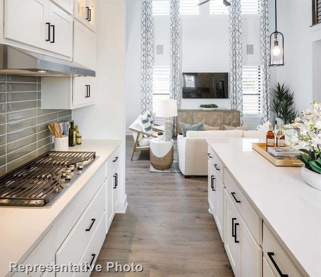 kitchen featuring dark wood-type flooring, under cabinet range hood, white cabinetry, light countertops, and stainless steel gas cooktop