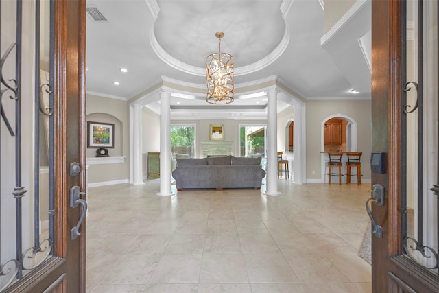 tiled foyer entrance featuring an inviting chandelier, a raised ceiling, crown molding, and ornate columns